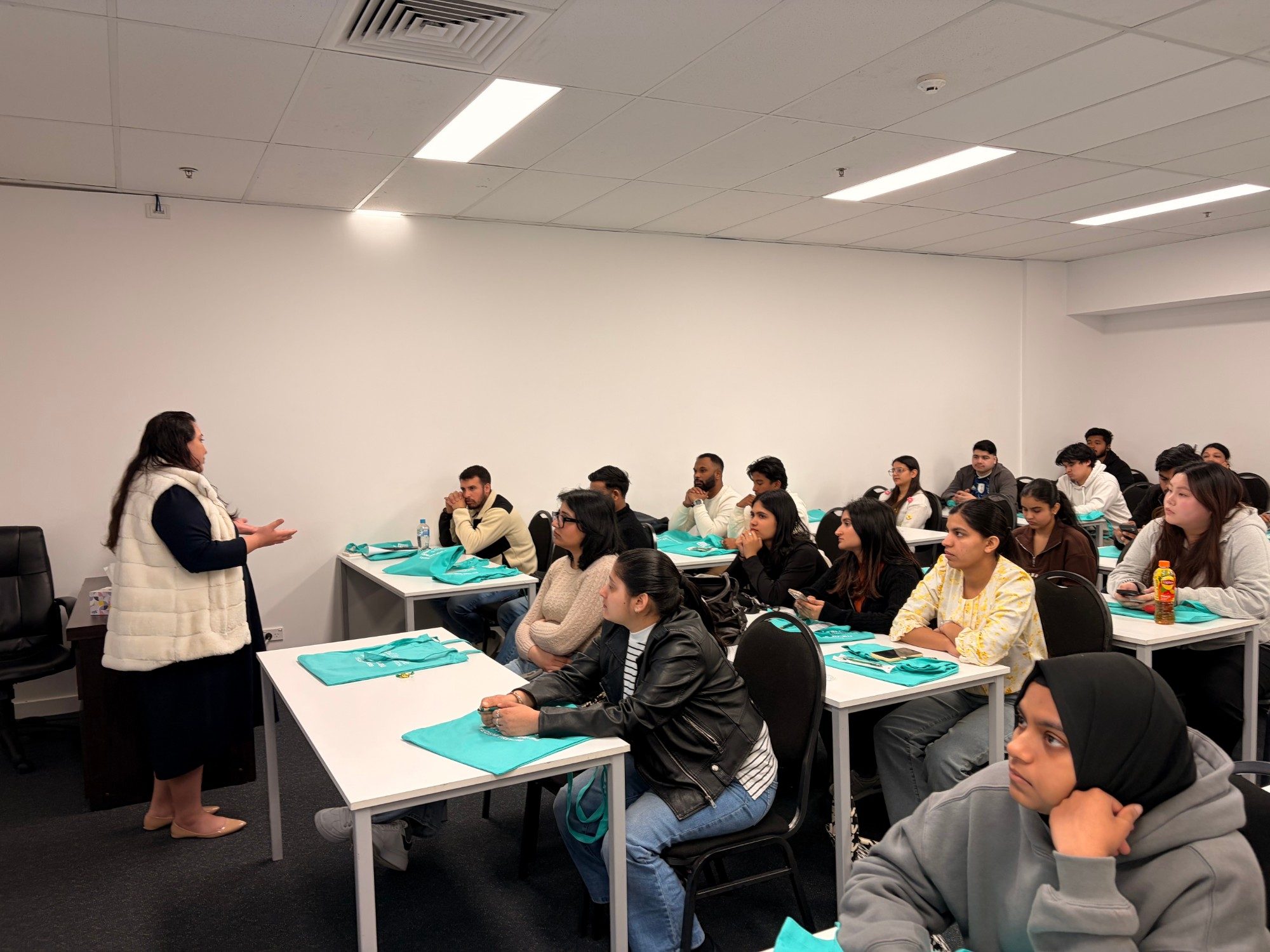 A LIHE staff member talking with a class of students seated at desks with LIHE tote bags