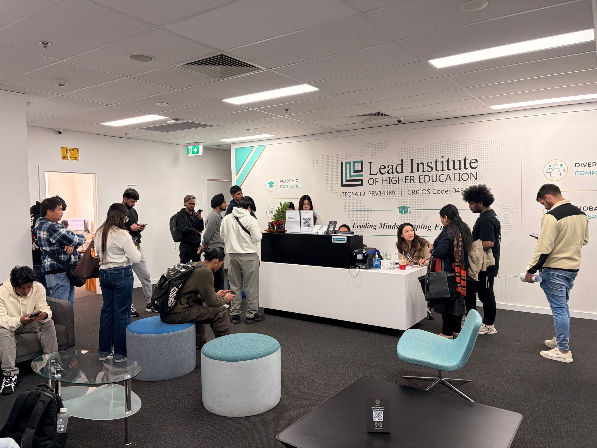 Students queueing at the LIHE reception desk while staff help them, with seating in the foreground