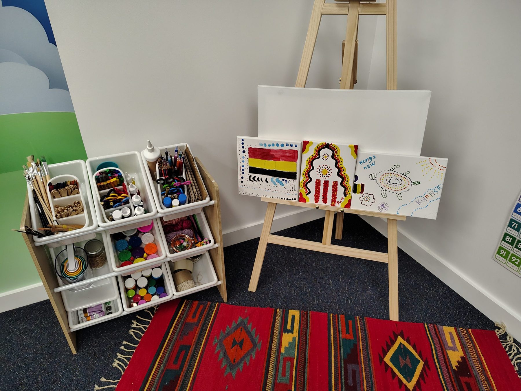 Art station in the simulation room, with an easel, paint cart and student artworks