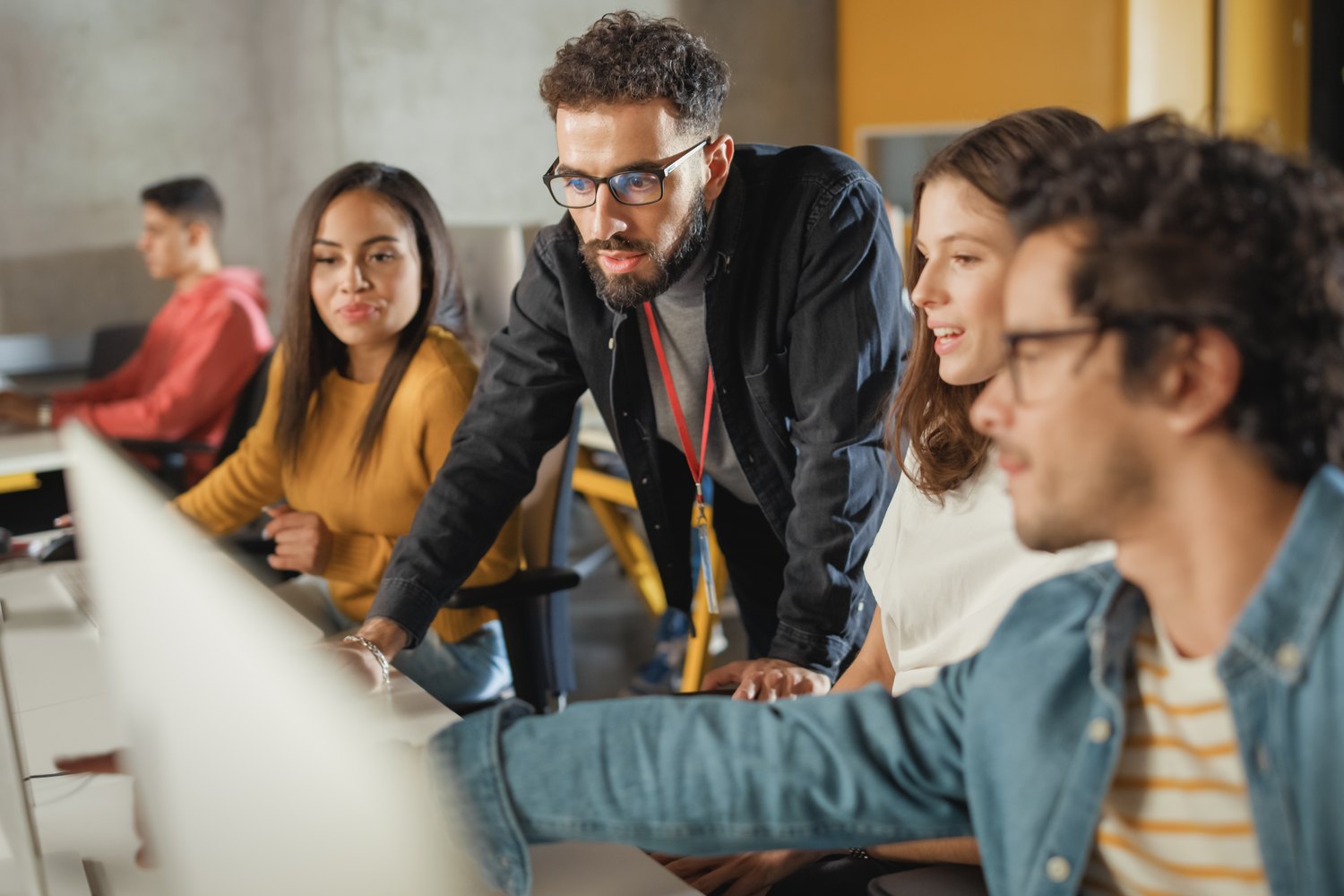 A tutor leaning over a desk to talk a small group of students through what is on their screen