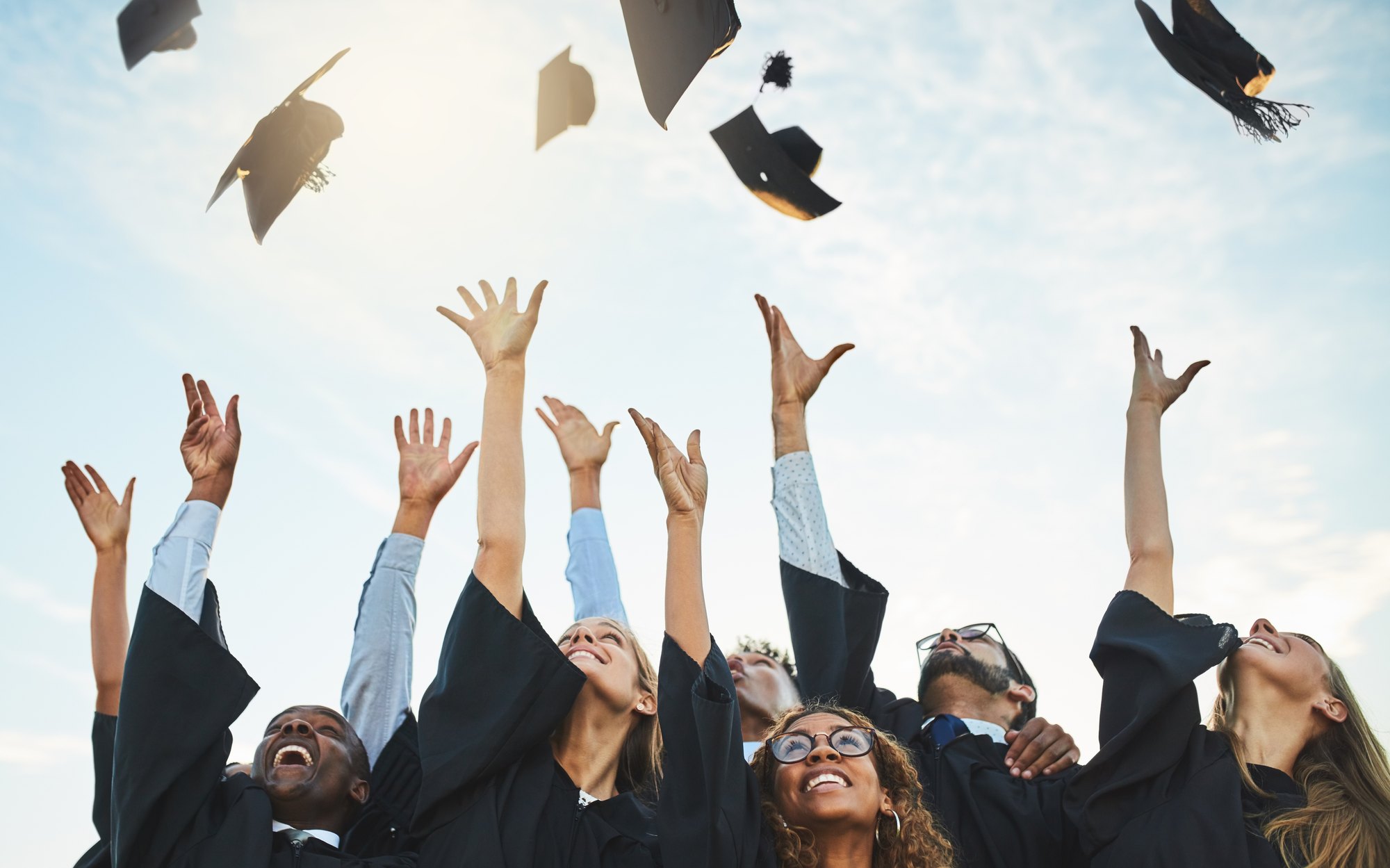 Graduates in gowns throwing their caps against an open sky